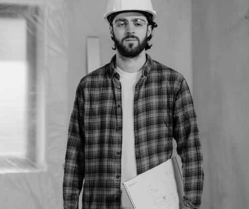 A construction worker with a hard hat and plaid shirt holding a blueprint inside a renovation site.